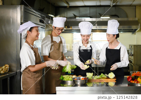 Group of culinary students in chef hats learning food preparation techniques Group of culinary students in chef hats learning food preparation techniques 125142828