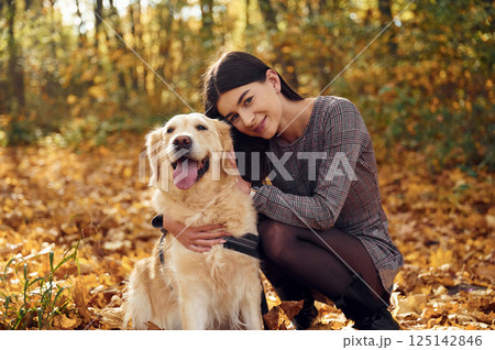 Sitting and smiling. Woman is on the walk with her dog in the autumn forest at daytime 125142846
