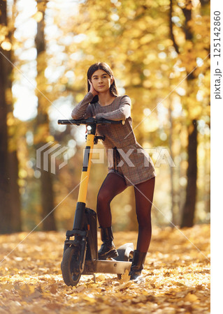 Standing and posing. Young woman is riding electric scooter in the autumn forest 125142860