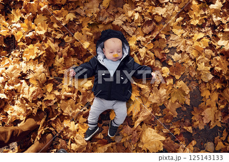Top view. Cute little baby is lying down on the ground with fallen leaves on it Top view. Cute little baby is lying down on the ground with fallen leaves on it 125143133