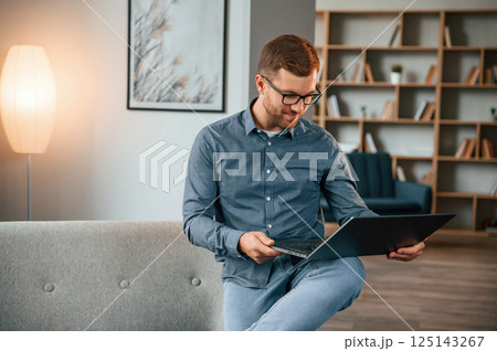 Male freelance worker in glasses is using laptop at home. Cozy apartment 125143267