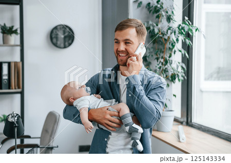 Having conversation by phone. Father with toddler is indoors in the office 125143334
