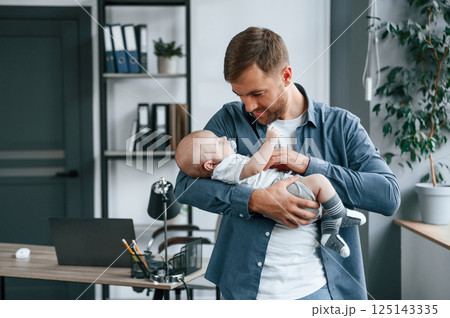 Looking at the baby. Father with toddler is indoors in the office 125143335