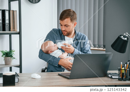 Looking at the baby. Father with toddler is indoors in the office 125143342