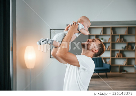 Smiling, having fun with baby is in the hands. Father with toddler is at home, taking care of his son 125143375