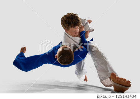 Momentum and control collide as white gi athlete performs rapid takedown, opponent fully lifted off ground, symbolizing technique against white background. 125143434