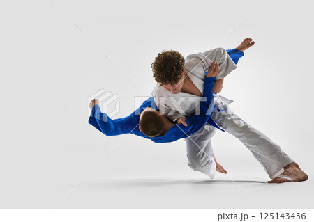 Dynamic mid-air twist as fighter in white unbalances opponent with strong stance, illustrating confidence, power against white background. 125143436