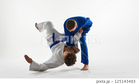 Decisive hip throw unfolding, white gi athlete launches opponent in controlled arc, embodying skill against white background. 125143483