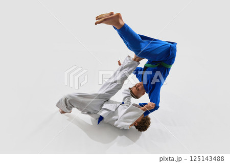 Action-packed takedown frozen mid-air, judoka in blue flipping over white gi opponent against white background, show strength. Action-packed takedown frozen mid-air, judoka in blue flipping over white gi opponent against white background, show strength. 125143488