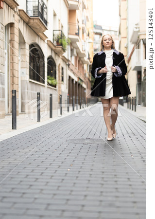 Happy woman in stylish dress walks along cobblestone street 125143491