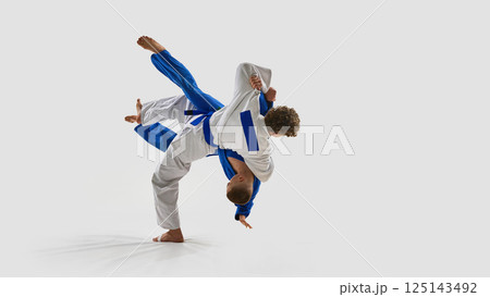 Energetic photo of judoka in white executes full-body rotation throw, opponent elevated off ground, representing precision against white background. 125143492