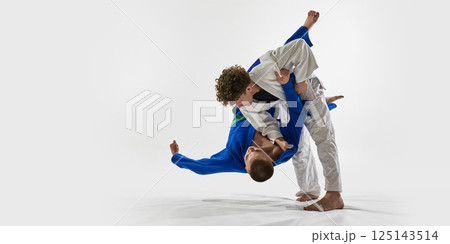 White gi fighter suspended mid-flip as opponent in blue initiates clean forward throw, demonstrating fluid motion,against white background. 125143514