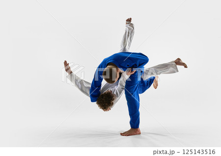 Blue gi fighter thrown over shoulder in fast motion by white gi athlete against white studio background. Concept of judo, combat sport 125143516