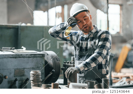 Tired factory male worker in uniform is indoors 125143644