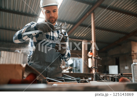 Measuring the object. Factory male worker in uniform is indoors Measuring the object. Factory male worker in uniform is indoors 125143869