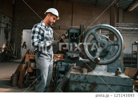 Metal processing. Factory male worker in uniform is indoors Metal processing. Factory male worker in uniform is indoors 125143893