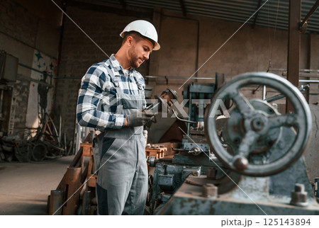 Metal processing. Factory male worker in uniform is indoors Metal processing. Factory male worker in uniform is indoors 125143894
