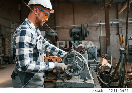 Focused on work with factory machine. Worker in uniform is indoors 125143921
