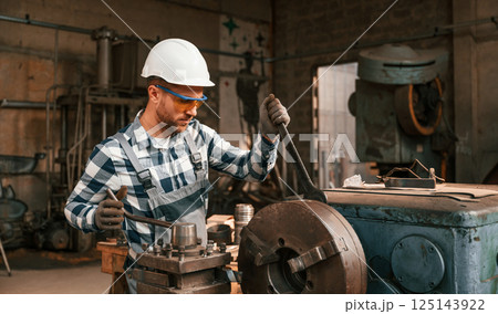 Focused on work with factory machine. Worker in uniform is indoors 125143922
