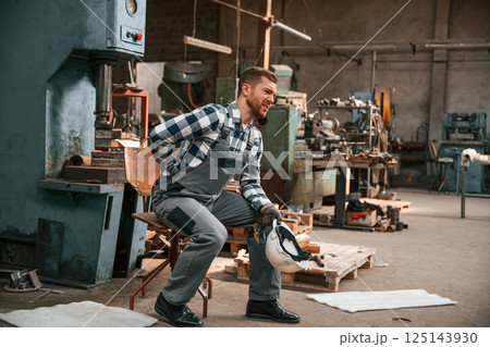 Felling bad. Back is hurting. Factory male worker in uniform is indoors Felling bad. Back is hurting. Factory male worker in uniform is indoors 125143930