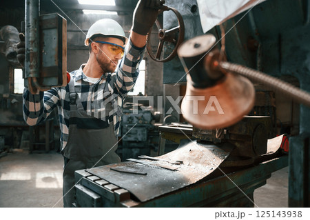 Operating the automatic driller. Factory male worker in uniform is indoors Operating the automatic driller. Factory male worker in uniform is indoors 125143938