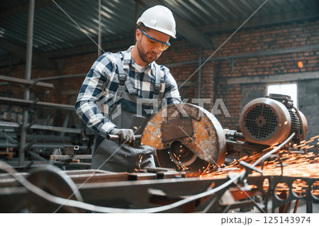 Many of the sparks. Cutting metal. Factory male worker in uniform is indoors 125143974