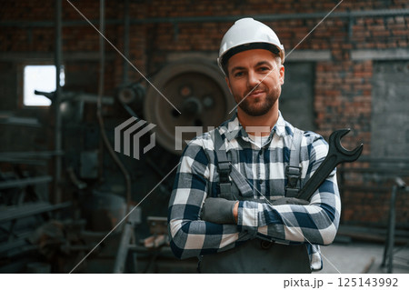 Smiling and holding wrench. Factory male worker in uniform is indoors 125143992