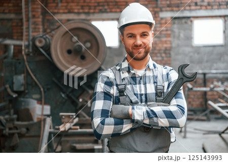 Smiling and holding wrench. Factory male worker in uniform is indoors 125143993