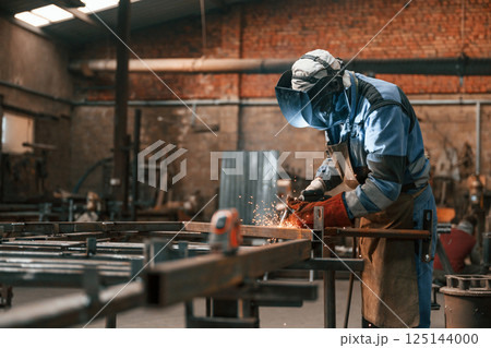 Factory worker in protective mask is welding the iron Factory worker in protective mask is welding the iron 125144000