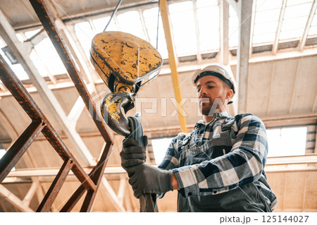 Working with crane. Man in a factory in uniform is indoors Working with crane. Man in a factory in uniform is indoors 125144027