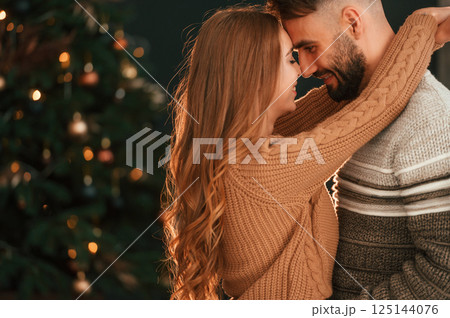 Standing and embracing. Lovely young couple are celebrating New Year at home 125144076