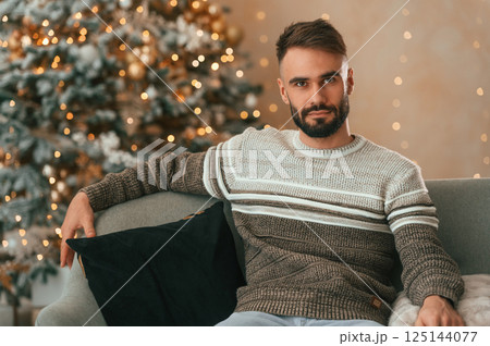 Beautiful young man is sitting on the sofa at New Year night at home 125144077