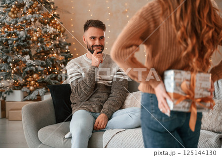 Man us guessing what gift he will receive from the woman. Lovely young couple are celebrating New Year at home 125144130