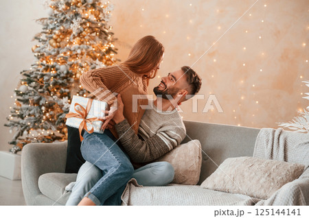 Woman is with gift box for the man. Lovely young couple are celebrating New Year at home 125144141