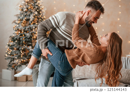 Man is holding leg of the woman while standing. Lovely young couple are celebrating New Year at home Man is holding leg of the woman while standing. Lovely young couple are celebrating New Year at home 125144143