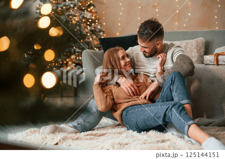 Sitting on the floor together. Lovely young couple are celebrating New Year at home 125144151