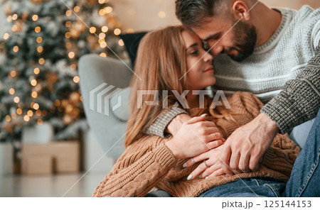 Laying down on the sofa and embracing. Lovely young couple are celebrating New Year at home Laying down on the sofa and embracing. Lovely young couple are celebrating New Year at home 125144153