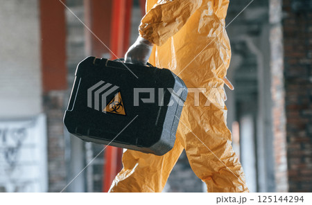 The case with biohazard sign on it. Man dressed in chemical protection suit in the ruins of the post apocalyptic building The case with biohazard sign on it. Man dressed in chemical protection suit in the ruins of the post apocalyptic building 125144294