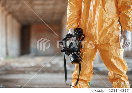 Holding gas mask. Man dressed in chemical protection suit in the ruins of the post apocalyptic building 125144317