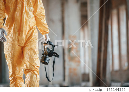 Respirator in hand. Man dressed in chemical protection suit in the ruins of the post apocalyptic building 125144323