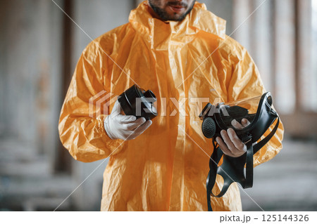Holding a respirator. Man dressed in chemical protection suit in the ruins of the post apocalyptic building 125144326