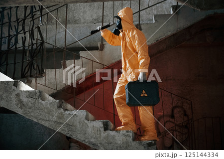 On stairs with flashlight and case. Man dressed in chemical protection suit in the ruins of the post apocalyptic building 125144334