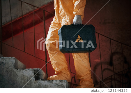 On stairs with flashlight and case. Man dressed in chemical protection suit in the ruins of the post apocalyptic building 125144335