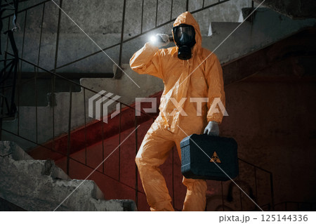 On stairs with flashlight and case. Man dressed in chemical protection suit in the ruins of the post apocalyptic building 125144336