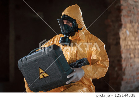 Sitting with radioactive case. Man dressed in chemical protection suit in the ruins of the post apocalyptic building 125144339