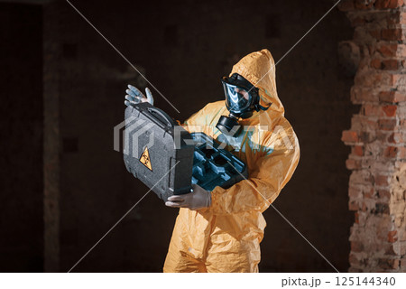 Case with blue glowing light. Hazard materials. Man dressed in chemical protection suit in the ruins of the post apocalyptic building 125144340