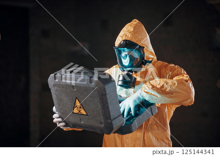 Case with blue glowing light. Hazard materials. Man dressed in chemical protection suit in the ruins of the post apocalyptic building 125144341