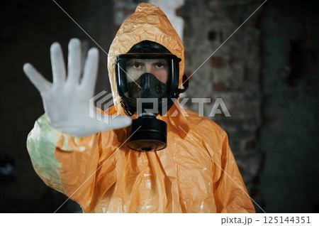 Stop sign by hand. Man dressed in chemical protection suit in the ruins of the post apocalyptic building 125144351