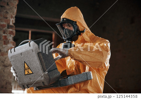 Sitting with radioactive case. Man dressed in chemical protection suit in the ruins of the post apocalyptic building 125144358