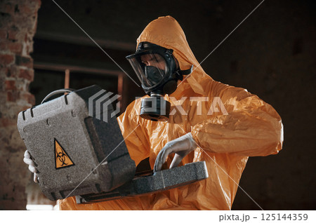 Sitting with radioactive case. Man dressed in chemical protection suit in the ruins of the post apocalyptic building 125144359